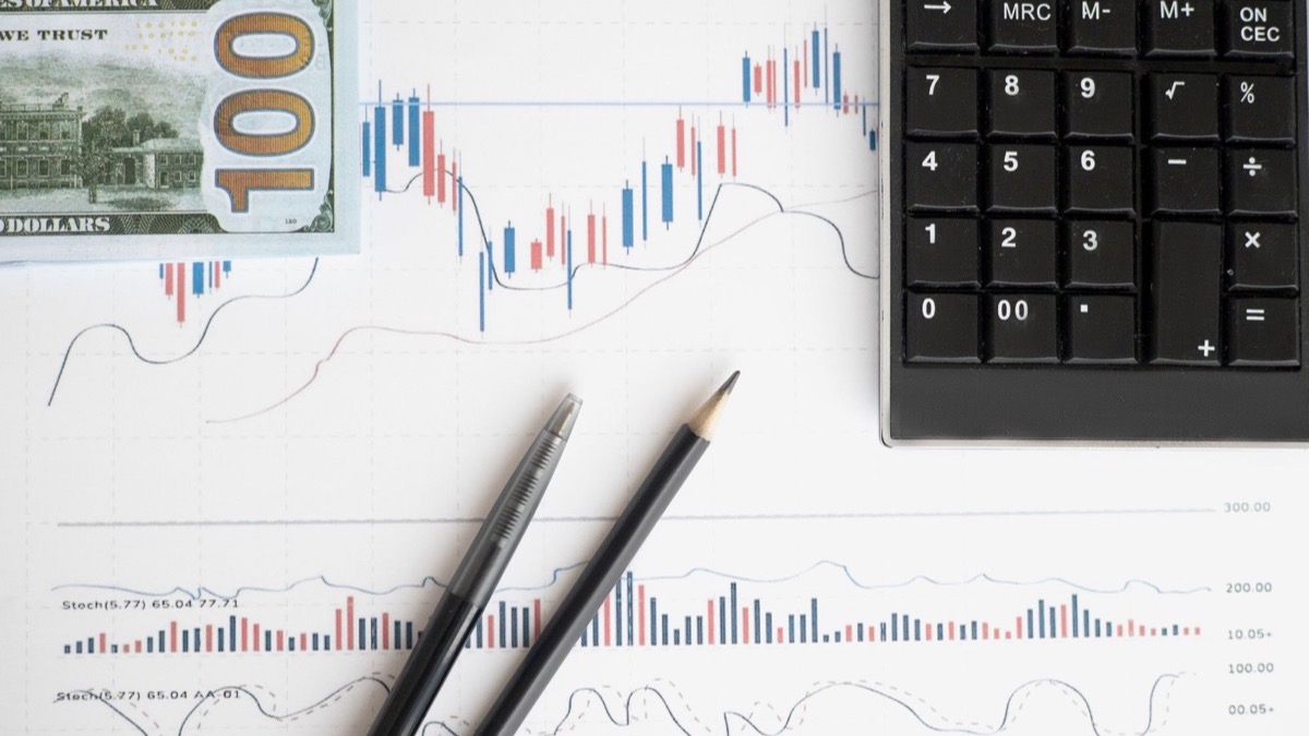 A desk with printed market charts, a calculator and banknotes