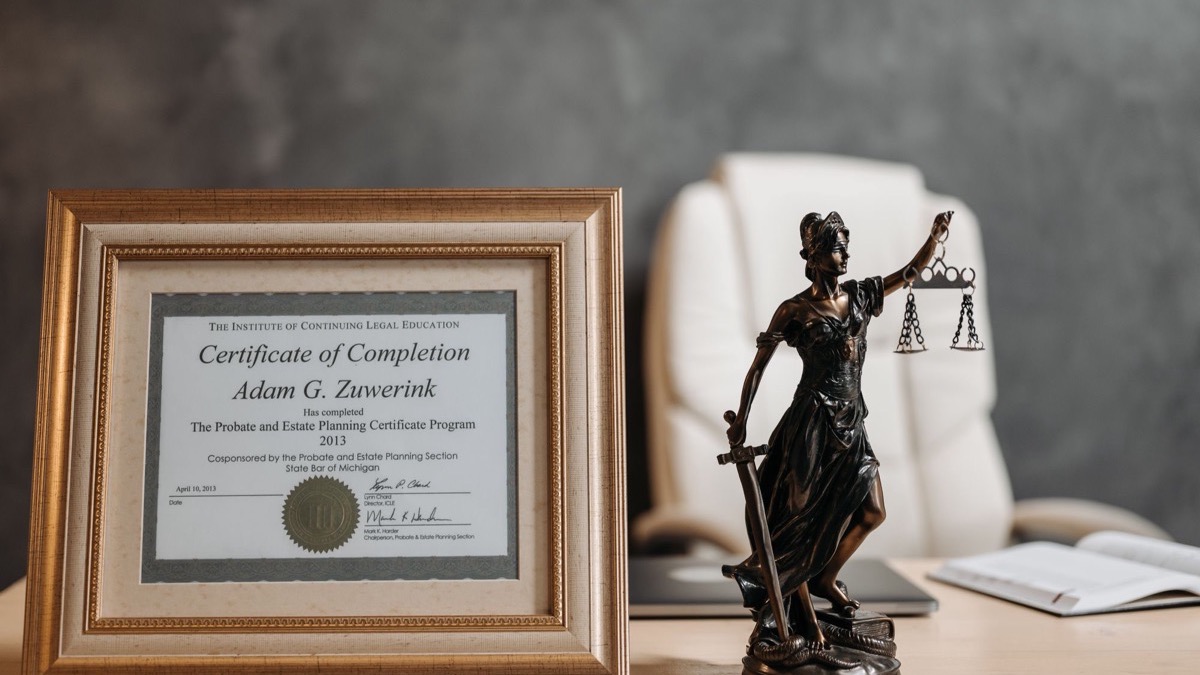 A framed certificate and a small figure of Lady Justice on a desk
