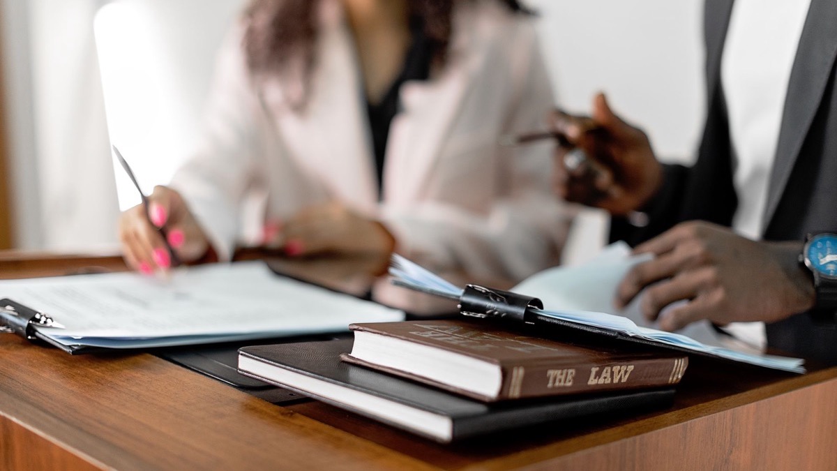 Two people reviewing documents at a desk stacked with law books