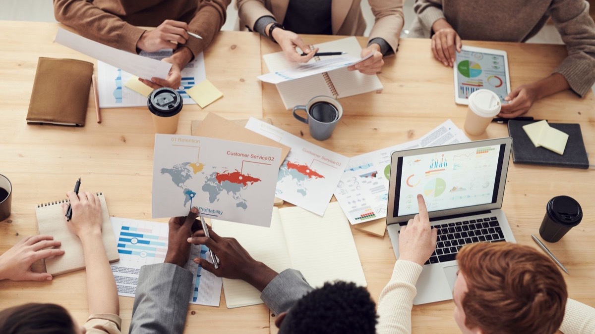 A team meeting with printed charts and laptops spread across the table