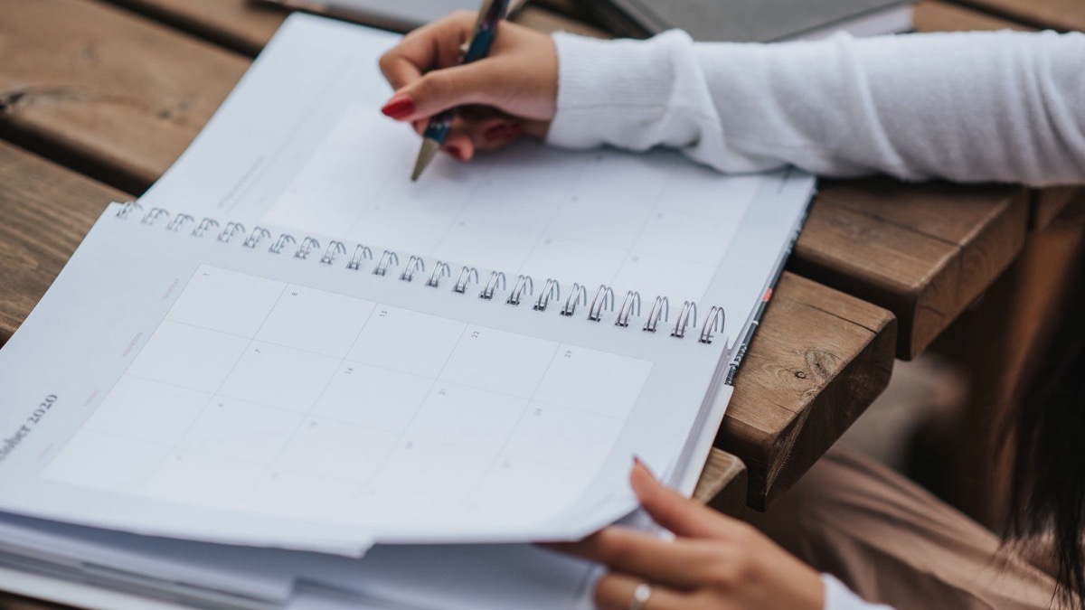 A student writing in a notebook while planning a study schedule