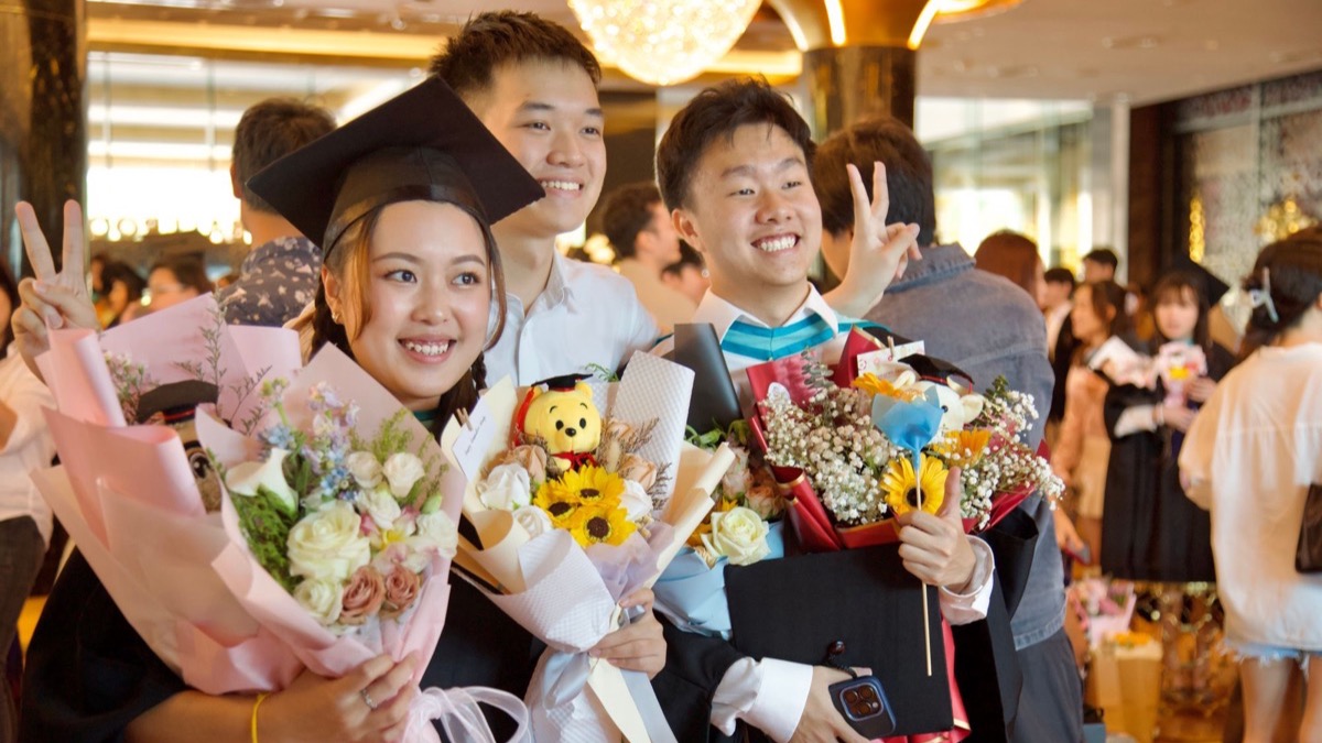 Ba tân cử nhân cùng chúc mừng nhau, trên tay cầm hoa