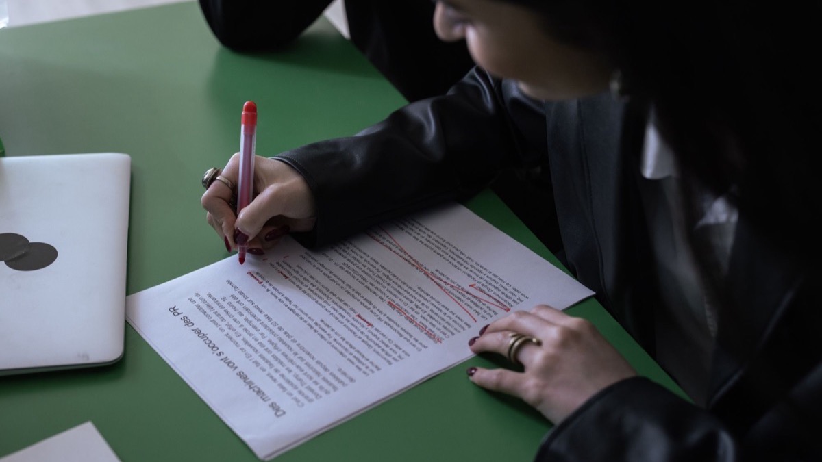 A person editing a printed document with a red pen at a desk