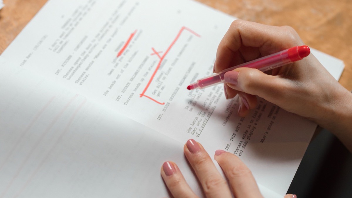 A hand marking corrections on a printed page in red